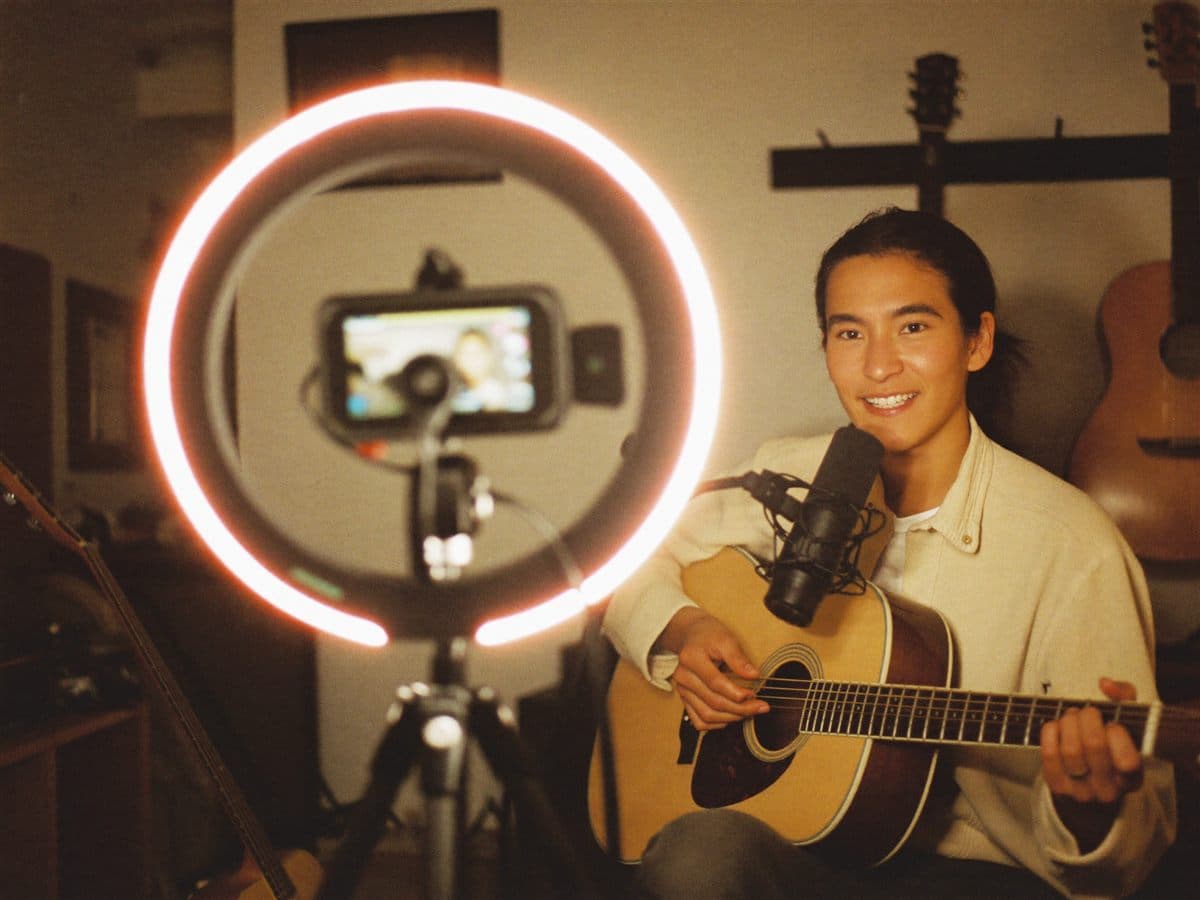 A guitar teacher recording an online lesson with a camera and ring light